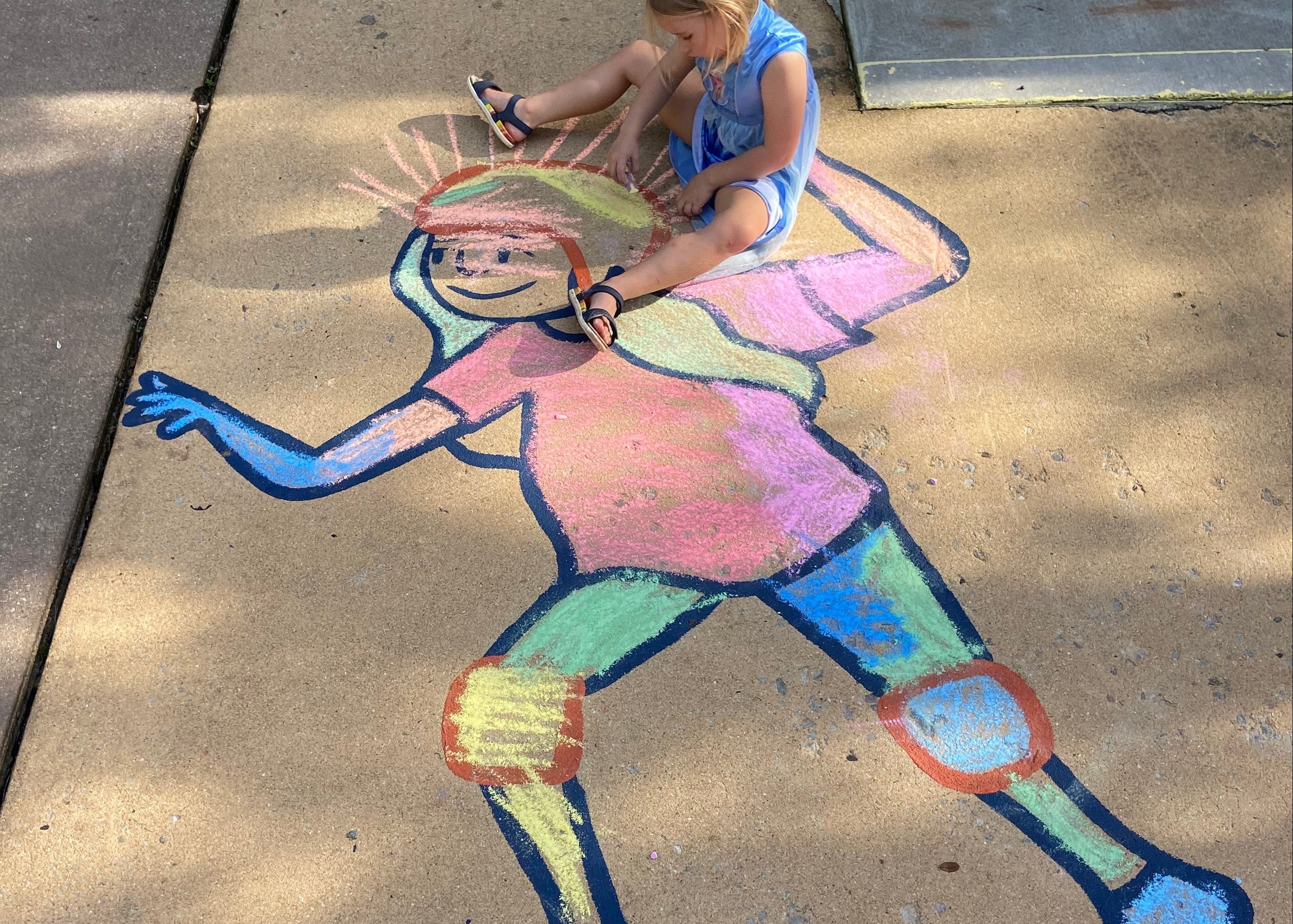 Colorful chalk drawing of a character on a sidewalk with a child sitting nearby.